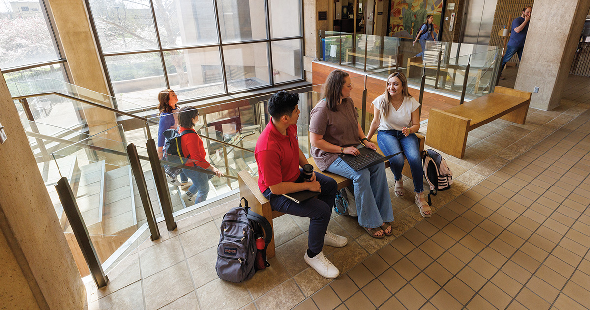 Three students chat on a bench at the top of the stairs at Green Hall