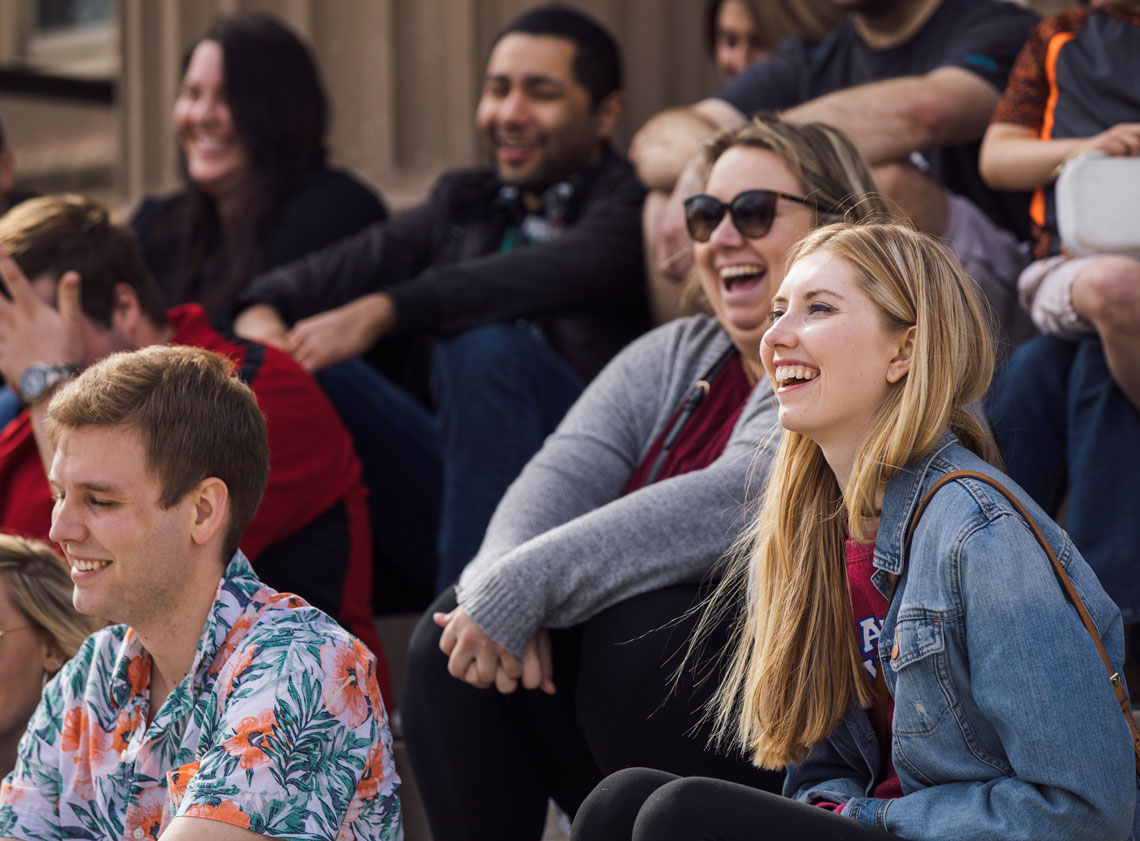 Students laugh while sitting on the front steps of a KU building