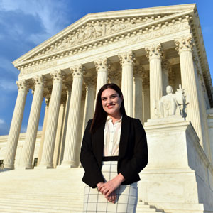 A female law student poses for a picture in front of the Supreme Court of the United States building.