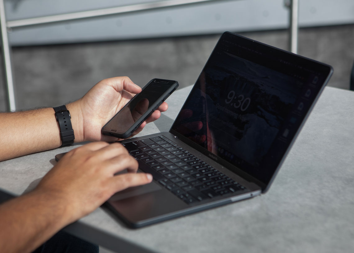 A student's hands are pictured with a phone and a laptop