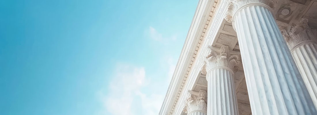 Upaward view of the columns of the U.S. Supreme Court Building framed by a blue sky.